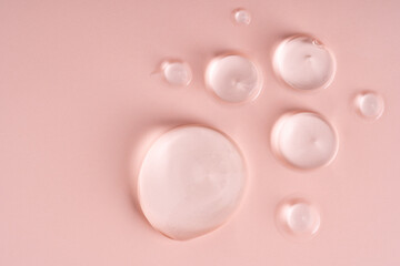Closeup of translucent gel droplets on a soft pink surface, highlighting the beautiful textures of skincare