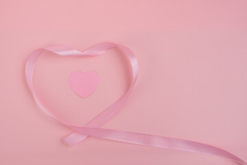 A pink ribbon forming a heart shape around a smaller pink heart