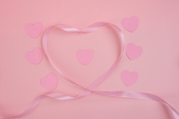 A pink ribbon forming a heart shape around smaller paper hearts