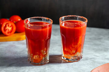 Two vegetable shaken cocktails in glass on dark grey background. Red tomato cocktail. Served with tomato slice. Vegan menu.