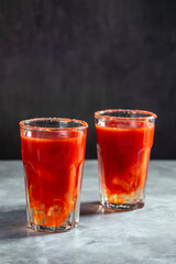 Two Bloody Mary cocktails in glass served with tomato slice and salt on dark background. Red cocktail. Alternative taste. Dirty dump drink
