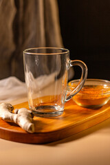 Empty transparent cup on wooden tray with turmeric and chili species. Mock up for design. Served table. Preparation for making drink