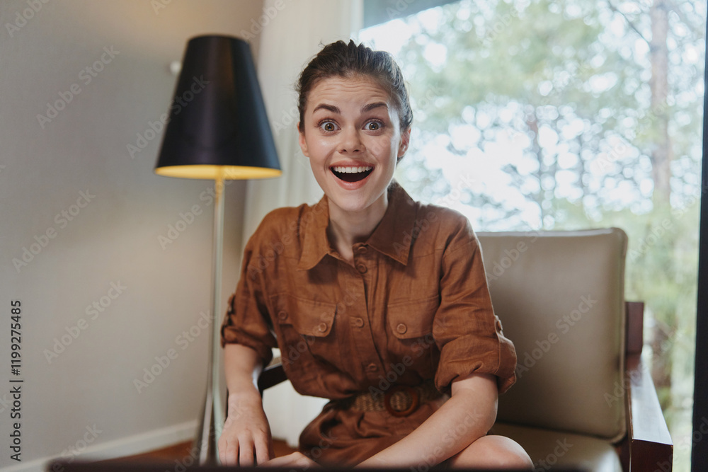 Canvas Prints Happy young woman smiling in a stylish brown outfit, sitting in a cozy room with natural light, conveying joy and positivity in a modern lifestyle context