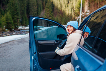 Portrait of woman admiring forest in mountains walking out of car looking at winter landscape....