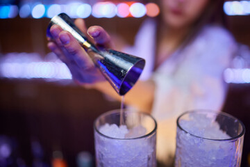 A skilled bartender expertly pouring a colorful cocktail into a series of waiting glasses