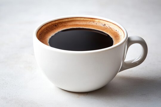 Rich, dark coffee fills simple white cup, showcasing creamy frot