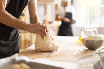 Baker's hands kneading raw dough in bakery