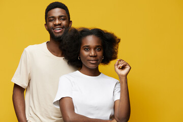 Fototapeta premium Two young Black adults smiling in front of a bright yellow background, showcasing friendship and joy in casual attire with natural hairstyles