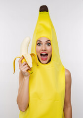 Happy woman smiling holding a peeled banana while dressed up in costume as a banana - isolated on white