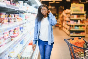 African American Female Customer Posing With Shop Cart Buying Food Products In Supermarket. Groceries In Store Concept