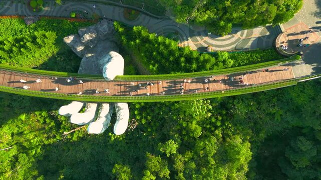 The Golden Bridge, supported by gigantic hands, stretches over lush greenery in Ba Na Hills, Vietnam, captivating visitors with its unique design and breathtaking scenery. Aerial drone view.