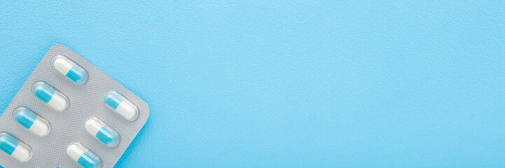 Blister pack of white blue pills on light blue table background. Pastel color. Closeup. Wide banner. Empty place for text. Top down view.