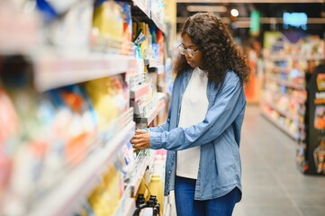 Interested young woman making purchases in household chemicals store, reading labels on bottles