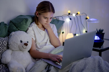 Cute Little Girl Typing On A Laptop In Bed Before Sleep, Surfing On The Internet