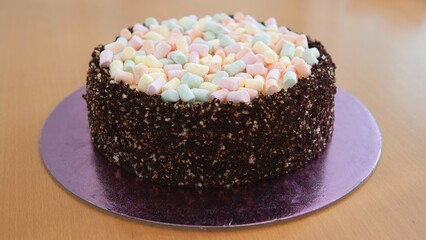 The photo shows a cake with brown edges and a light top. Marshmallows of different colors are present on top of the cake.