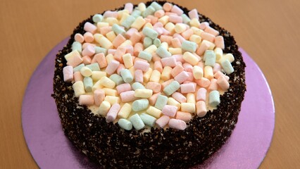The photo shows a cake with brown edges and a light top. Marshmallows of different colors are present on top of the cake.