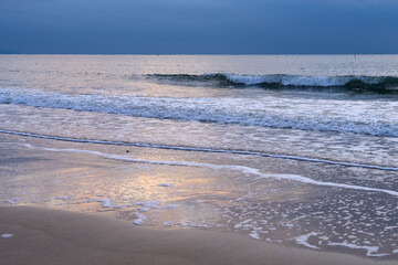 tranquil seascape with surfs on the beach during sunset