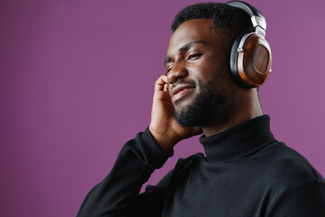 Young Black man enjoying music with headphones against a purple background, expressing happiness and relaxation in a modern, stylish setting