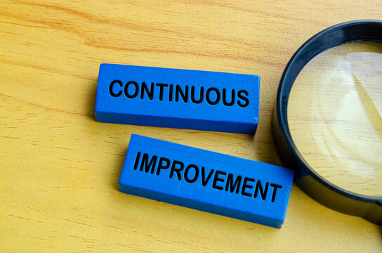 Top view of continuous improvement text on blue wooden blocks with magnifying glass background. Continuous improvement concept