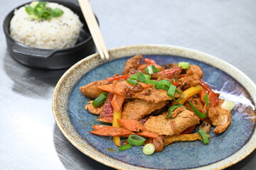 A vibrant and spicy Korean-style dish featuring tender pork, fresh vegetables, and steamed rice, beautifully plated in a restaurant setting.