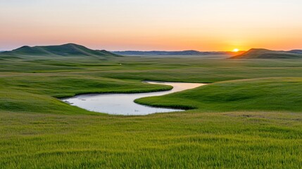 Fototapeta premium Serene sunset over a meandering river in a vast green prairie landscape.
