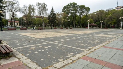 A large empty square in a city park with a faded color scheme and peeling asphalt, empty space, concrete, overgrown weeds, urban decay, abandoned playground