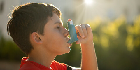 Boy using an asthma inhaler outdoors, focusing on respiratory health and inhaler usage. Close-up of...