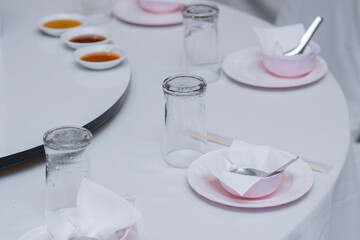 A dining table covered with a white tablecloth for an event with plates, cups, spoons and glasses arranged in an orderly manner.