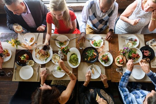 Diverse friends dining together, sharing food and drinks. Overhead view of people enjoying a meal, socializing, and celebrating around a table with various dishes. Friends having dinner at restaurant.