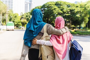 Two Muslim girls walking arm in arm, wearing colorful hijabs. Friendship and support. Outdoor scene with trees and a road. Unity and companionship. Muslim women embrace while walking outdoor
