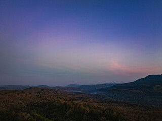 Aerial view A breathtaking sunset paints the sky with vibrant hues of orange and red, .casting a warm glow over the majestic mountains in a tranquil evening landscape.
