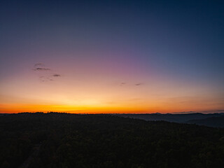 Aerial view A breathtaking sunset paints the sky with vibrant hues of orange and red, .casting a warm glow over the majestic mountains in a tranquil evening landscape.