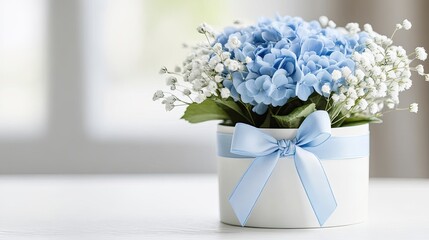 A round white gift box holds a stunning blue hydrangea and delicate baby's breath bouquet, beautifully wrapped and placed on a table