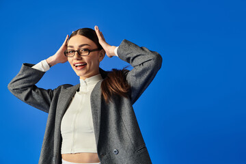 A young woman in a chic outfit playfully interacts against a blue backdrop.