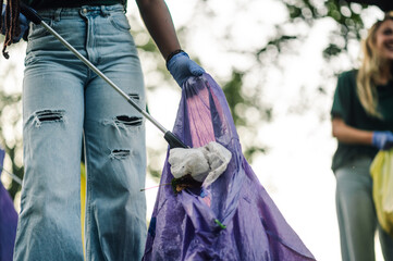 Volunteer picking up trash in park holding purple garbage bag