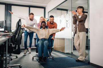 Naklejka premium Cheerful business team pushing a colleague on an office chair