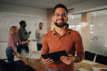Smiling businessman holding tablet with coworkers discussing in background