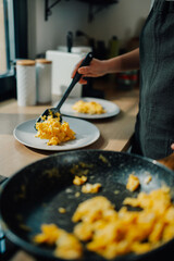 Chef serving scrambled eggs from frying pan onto plate in kitchen