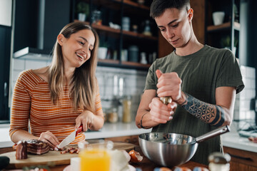 Young lesbian couple preparing food and smiling in kitchen