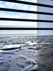 Rain droplets on a balcony surface after a shower, reflecting the sky and creating a peaceful mood. Perfect for themes like tranquility, nature, rain, and stillness in everyday moments.