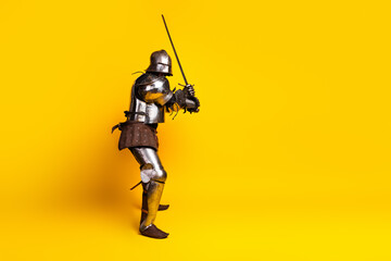 Medieval Knight in Steel Armor Posing with Sword Against Vibrant Yellow Background