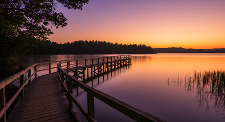 Fototapeta premium Wooden walkway into the lake with natural scenery of sunset and silhouette of forest in background