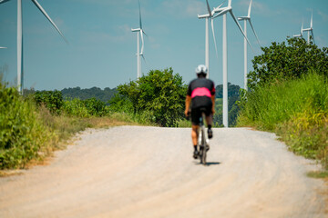 Obraz premium Cyclist rides along dusty path near wind turbines on a sunny afternoon in rural area