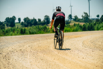 Obraz premium Biker navigating a gravel road surrounded by green fields on a sunny day
