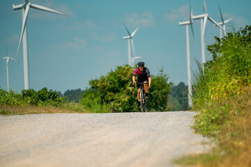 Obraz premium Bicyclist rides along gravel path near wind turbines on a sunny day in a rural landscape
