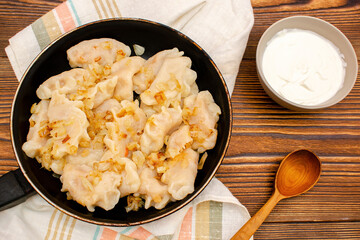 Homemade dumplings,vareniki,varenyky,pyrohy with stewed cabbage fried,onion on pan.Traditional ukrainian popular national dish,cuisine served with sour cream on wooden board.