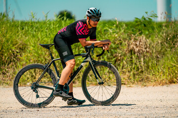 Fototapeta premium Cyclist resting on gravel road near open fields during daytime ride