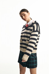 A young woman showcases her emotions while dressed in a stylish striped sweater and plaid skirt.