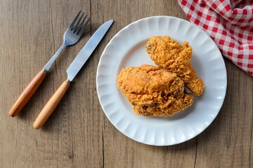 Fried chicken with knife and fork in a white plate on wooden background, top view
