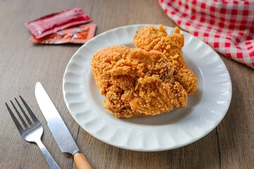 Fried chicken with knife and fork in a white plate on wooden background, top view